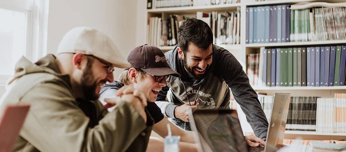 Group of diverse young professionals collaborating on a laptop in a library setting.