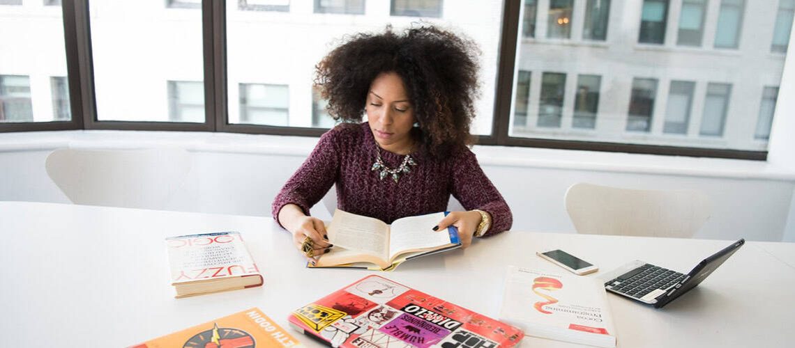 Woman reading a book about personal values and branding at a modern office desk.