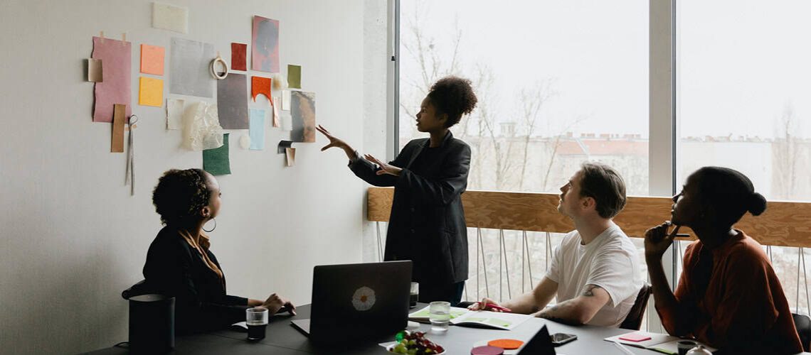 Woman presenting a book outline to a diverse team in a modern office setting.