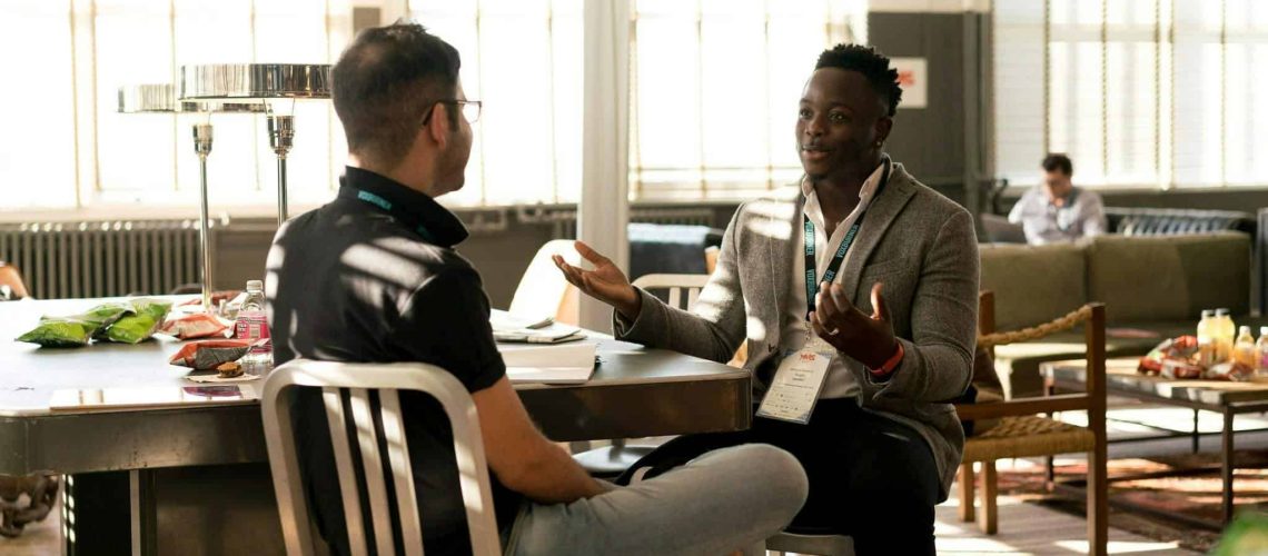 Two diverse writers engaging in a discussion at a conference table.