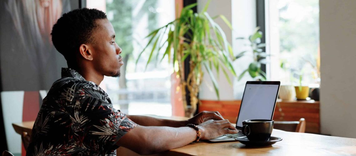 Woman working on laptop at coffee shop with natural light and greenery.
