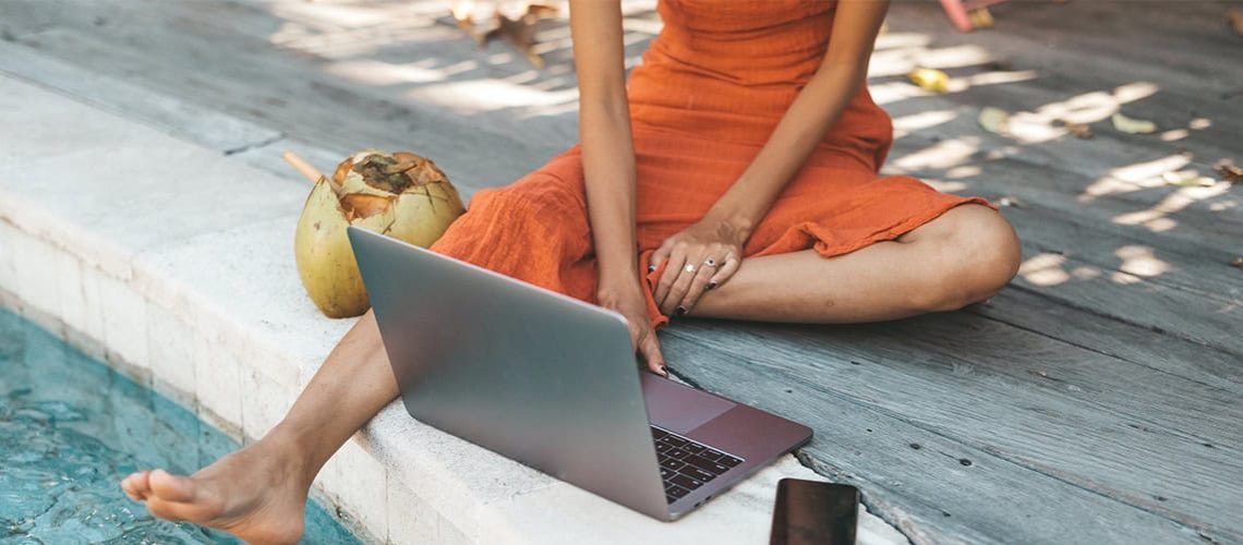 Woman working on a laptop by the pool with coconuts, relaxing outdoor setting.